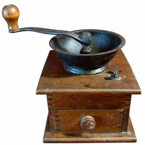 An antique wooden box coffee grinder isolated on a white background, featuring a dark cast iron hopper bowl, a hand crank with a wooden knob, and a closed small drawer at the bottom.