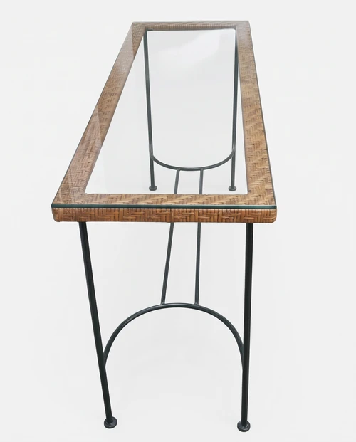 Overhead perspective looking down length of clear glass console table framed in natural woven rattan on stone terrace