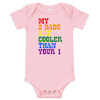 Pink baby bodysuit with the bold phrase "MY 2 DADS ARE COOLER THAN YOUR 1" in vibrant rainbow colors, celebrating same-sex parents with humor and love.