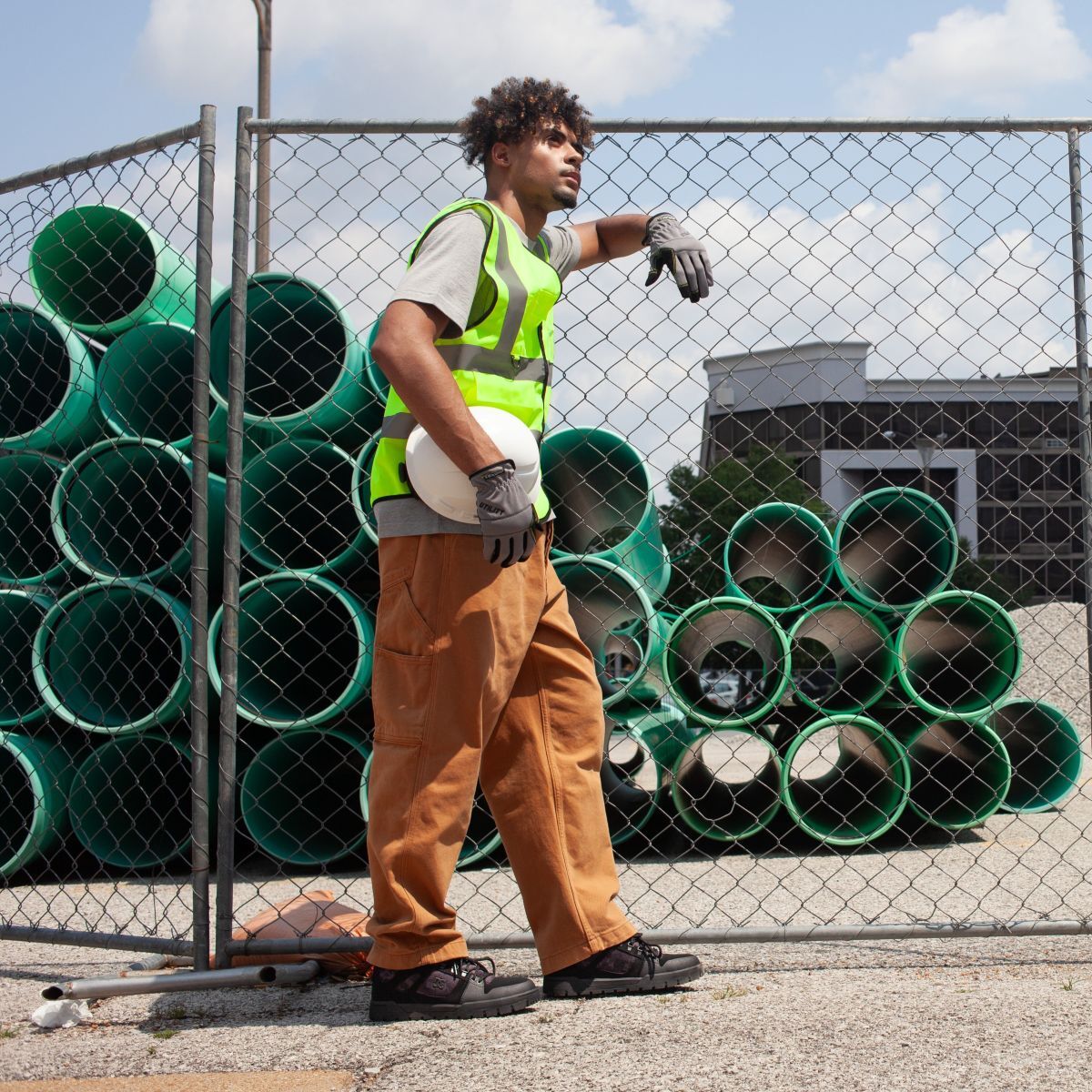 Construction worker, wearing DC60603 safety shoes, leaning on a chain link fence at the jobsite