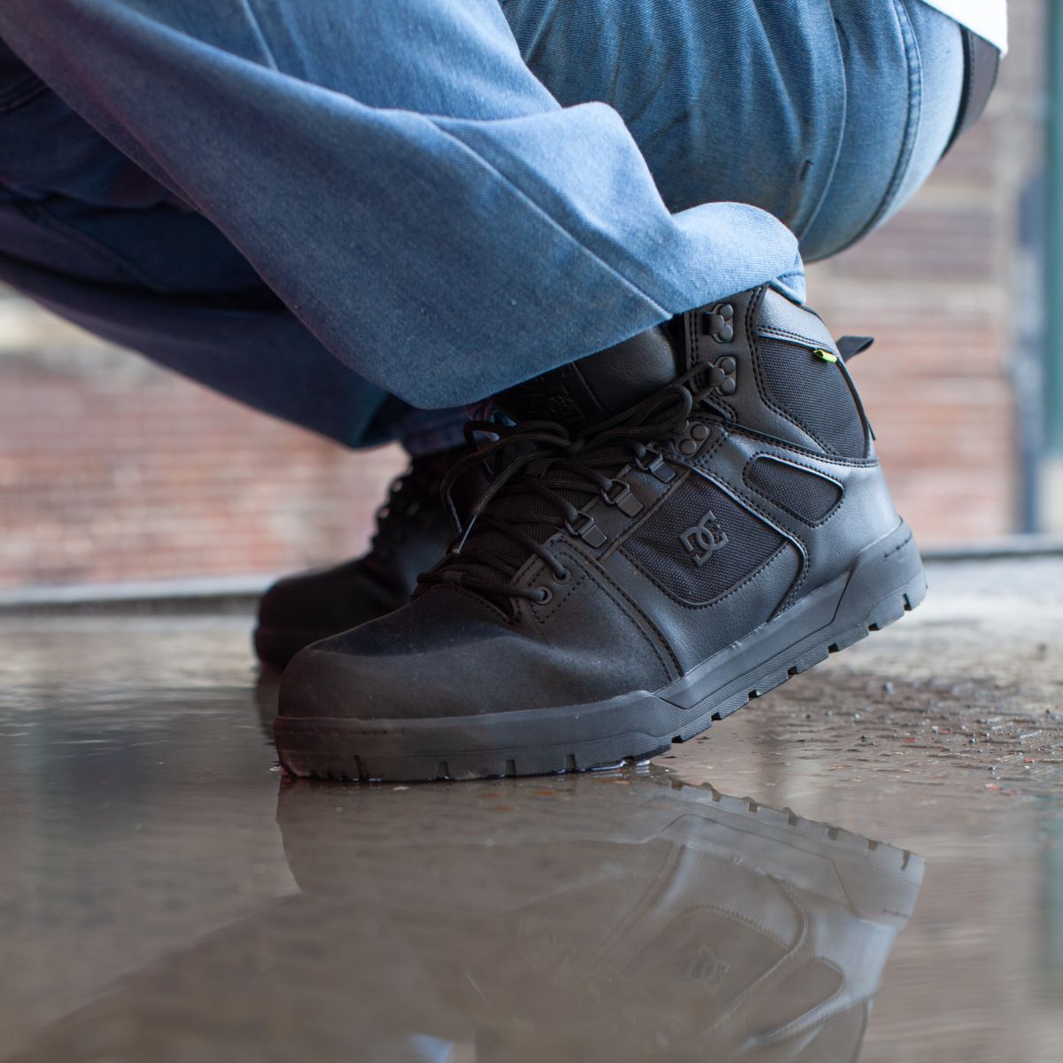 Man wearing DC60604 slip resistant shoes is squatting in a puddle on a concrete floor