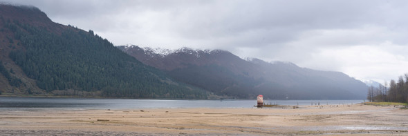 a panoramic view of an old saltwater pump house on a sandy beach with mountains across the inlet
