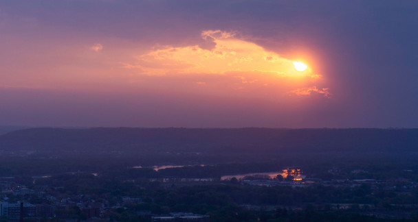 Yellow sun just breaking through a canopy of purple clouds overlooking the city below