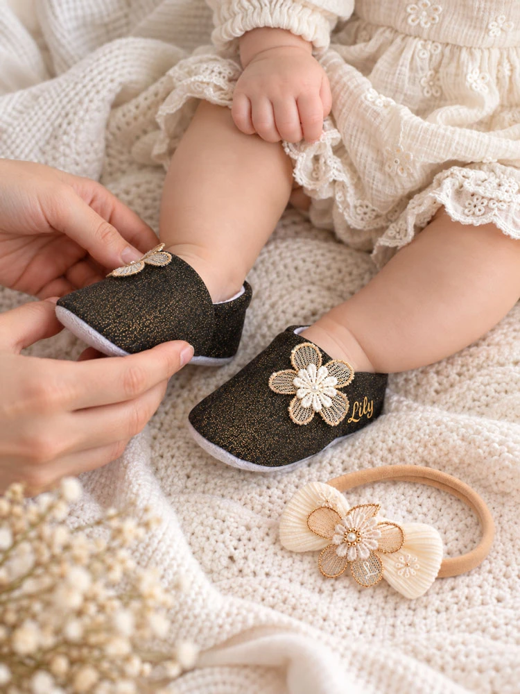 Baby wearing personalised black and gold pre-walker shoes with matching Blossom & Lace floral headband