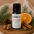 Tis The Season Essential Oil Blend by Essential7, featuring Nutmeg, Cinnamon Bark, Sweet Orange, and Spruce in Organic Sunflower Oil, styled with festive evergreen, orange, cinnamon, nutmeg, and pine cone accents.
