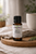 A warm, natural product photo of an amber glass bottle labeled Bee’s Knees Essential Oil Blend by Essential7. The bottle sits on a round wooden board with soft beige linen, gentle natural light, and a blurred neutral background. The label highlights Knee Comfort & Movement Support, creating a calm, grounded, Wisdom by Nature feel.