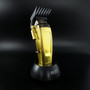 A three-quarter view of the gold Saber 2 cordless hair clipper in its charging dock, showing the adjustable taper lever and side controls.