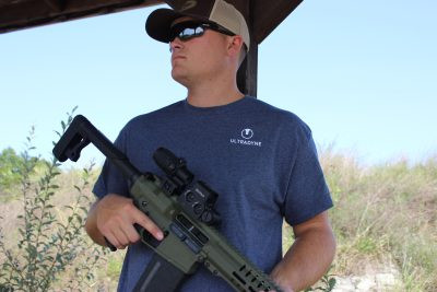man holding rifle, wearing Ultradyne t-shirt 