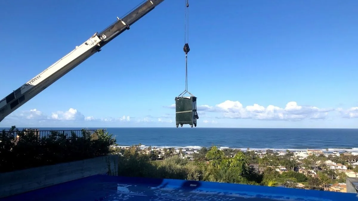 Boswell moving a safe by crane over a pool with an ocean view in the background