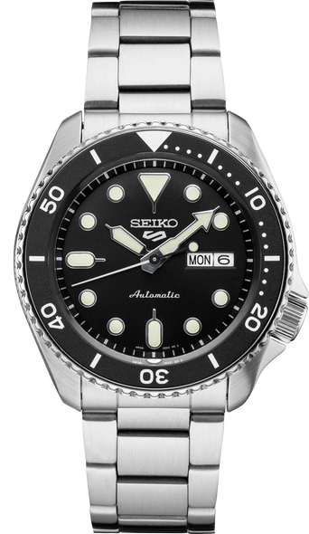 This is a new Seiko automatic 5 Sports watch that features a Seiko 24 jewel automatic (self-winding, hand wind, hacks) movement. The black dial has a day and date display at 3:00, highly luminous hands and markers treated with Lumibrite for low light visibility, an offset crown at 4:00, a uni-directional rotating bezel, a Hardlex mineral crystal and an exhibition window screw-down case back. 42.5mm diameter stainless steel case. It comes on a stainless steel bracelet with a deployant clasp. Manual and Seiko box are included