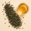 Darjeeling FTGFOP1 loose leaf black tea with a cup of golden amber brewed tea on a warm cream background.