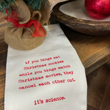 A white towel on a dark wood surface next to a miniature fir tree. In red type writer letters reads "if you binge eat Christmas cookies while you binge watch Christmas movies, they cancel each other out. it's science." on the towel.