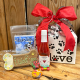 white gift box with paw prints in black and a red bow, with contents of gift displayed on a wood table. Contents list in product discription,