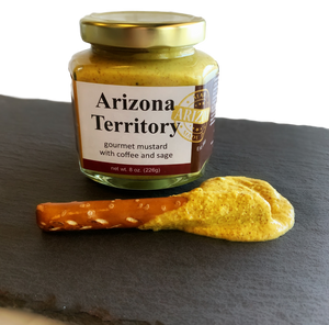 Round glass jar with gold lid containing yellow colored mustard with a pretzel rod dipped in mustard laying in front. Round glass jar with gold lid containing yellow colored mustard with a pretzel rod dipped in mustard laying in front.