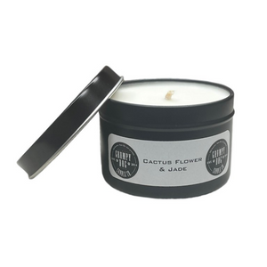 Candle in a round black tin with lid and white label with black lettering