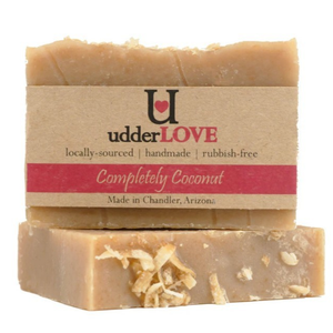 Tan bar of soap with flakes of coconut on top and with tan paper wrapping for a label with dark pink writing