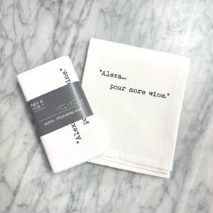 a marble countertop with a white towel laying on top on it, folded in half reading " ' Alexa ... pour more wine' " in a typewriter font. Next to the towel is the folded version of the same towel with a gray band around it with the Dev D and Co. logo