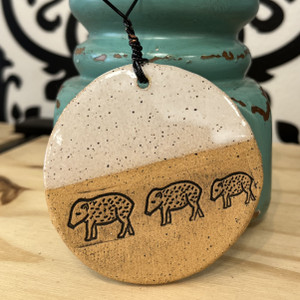 Round ceramic ornament with the top painted white and the bottom in natural clay color with three small javelinas carved in.