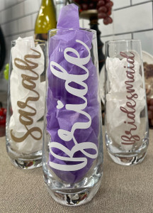 Three stemless champagne flutes, two behind and one in front. The two in the back read "Sarah" and "Bridesmaid". The one in front reads "Bride". All in cursive font horizontally down the glass