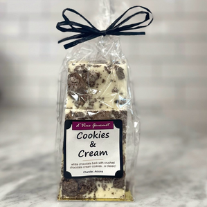 Clear cello food packaging showing contents of white chocolate bark with bits of dark cookie with square front label and tied with a bow