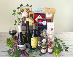 A brown wooden basket with products in and in front of it. Vine and grapes decorate the basket.