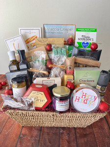 A woven brown basket with burgundy filling and products standing in it. Red ornaments are placed in and around the basket.