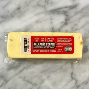 a marble countertop with a pale yellow colored cheese with flecks of red and green peppers. A red label reading the product information