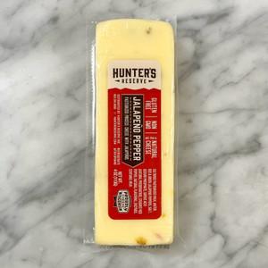 a marble countertop with a pale yellow colored cheese with flecks of red and green peppers. A red label reading the product information