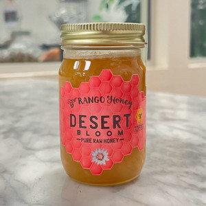 Small, oblong glass jar with a gold lid. a pink honeycomb-like label reads the company name and product flavor