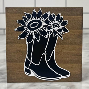Square wood block with a pair of black cowboy boots with sunflowers coming out from the top of the boots