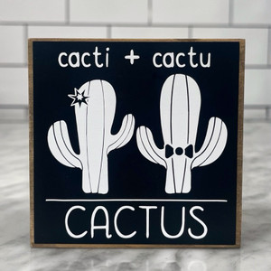 Square wood block with black background with white lettering and a white cactus with a star and another white cactus with a bowtie.
