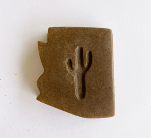 dark brown bar of soap in the shape of Arizona with a cut out shape of a saguaro cactus in the middle