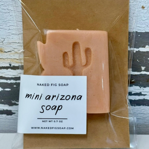 Tan bar of soap in the shape of Arizona with an imprint of a cactus in the center, on a brown background wrapped in clear plastic and a small white label