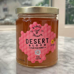 Round clear glass jar with gold lid containing golden honey with label shaped like a honey comb