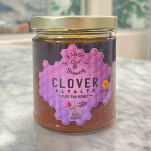 clear glass jar with silver lid containing golden honey with purple front label with honey comb pattern