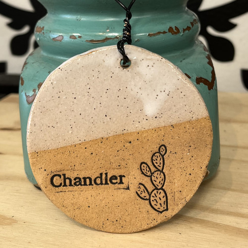 half off-white and half natural clay in color. circle shape. bottom half with natural clay color depicts a prickly pear cactus and the city name "Chandler" stamped into it