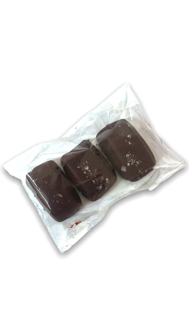 A clear packaging showing three dark chocolate covered caramels topped with coarse sea salt A clear packaging showing three dark chocolate covered caramels topped with coarse sea salt