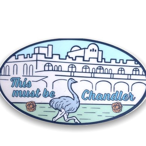 Oval sticker with image of Downtown Chandler buildings, ostrich and tumbleweeds in shades of light blues, pink and green.