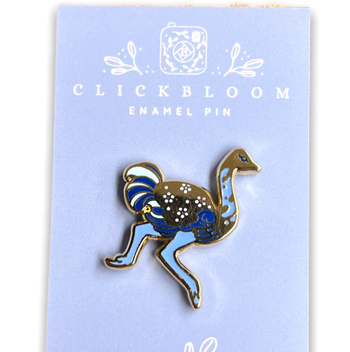 Enamel pin in the shape of a ostrich in shades of blue and gold.