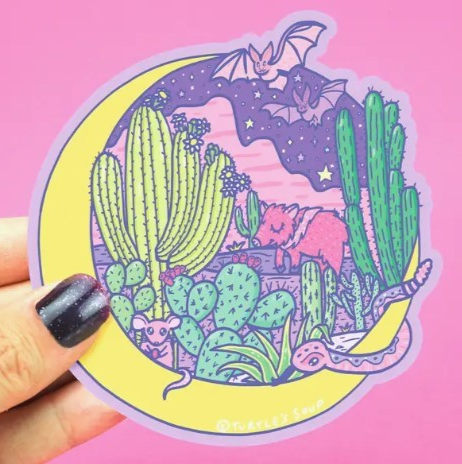 Round sticker featuring a yellow crescent moon on the left and one the right is a desert landscape featuring different cacti and creatures such as bats, javelinas, and snakes