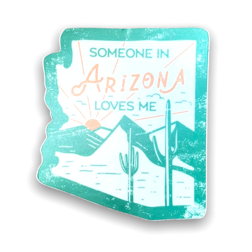 Sticker in the shape of the state, Arizona, displaying a desert landscape and the sun peaking over a mountain. Within the sun rays it says "Someone in Arizona Loves Me"