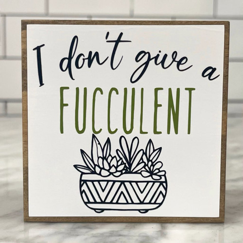 Square wood block with white background, black and green lettering, and a drawing of a pot of succulents. 