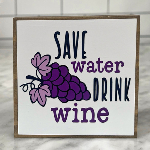 Square wood block with white background, black and purple lettering and image of a bunch of purple grapes. 