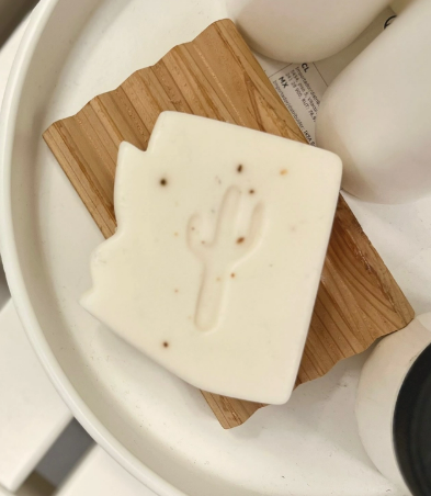 off white bar of soap in the shape of Arizona with a cut out in the shape of a saguaro cactus displayed on a wood soap saver dish