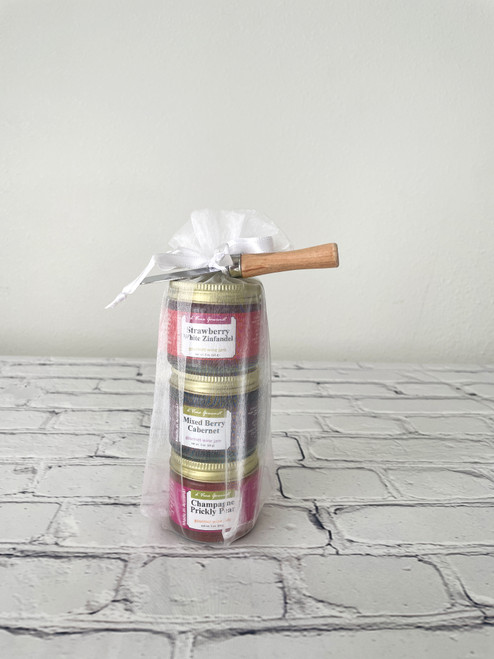 Three jars of jelly with a spreader in a decorative bag