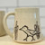 Light tan mug with handle with drawing of roadrunner and cacti