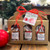 A linen patterned gold cardboard box with three arched windows on the front. Each window has a bag of caramels showing: one with Hot Chocolate Caramels, one with Classic Sea Salt Caramels, and one with Gingerbread Caramels. Box is tied with a red bow and a gift tag reading "Happy Holidays" A linen patterned gold cardboard box with three arched windows on the front. Each window has a bag of caramels showing: one with Hot Chocolate Caramels, one with Classic Sea Salt Caramels, and one with Gingerbread Caramels. Box is tied with a red bow and a gift tag reading "Happy Holidays"