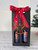 A tall, black gift box with two arched windows in the front. The Arizona Angel winery logo is visible through the windows. The box is tied with a red ribbon reading "made in Arizona." An iron angel wings ornament hangs from the box. A green Christmas tree is in the background. A tall, black gift box with two arched windows in the front. The Arizona Angel winery logo is visible through the windows. The box is tied with a red ribbon reading "made in Arizona." An iron angel wings ornament hangs from the box. A green Christmas tree is in the background.