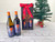 Two wine bottles with Arizona Angel winery logos on them are in front of a tall, black gift box with two arched windows in the front. The Arizona Angel winery logo is visible through the windows. The box is tied with a red ribbon reading "made in Arizona." An iron angel wings ornament hangs from the box. The box is in front of a green Christmas tree. Two wine bottles with Arizona Angel winery logos on them are in front of a tall, black gift box with two arched windows in the front. The Arizona Angel winery logo is visible through the windows. The box is tied with a red ribbon reading "made in Arizona." An iron angel wings ornament hangs from the box. The box is in front of a green Christmas tree.