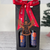 A tall, black gift box with two arched windows in the front. The Arizona Angel winery logo is visible through the windows. The box is tied with a red ribbon reading "made in Arizona." An iron angel wings ornament hangs from the box. A green Christmas tree is in the background.